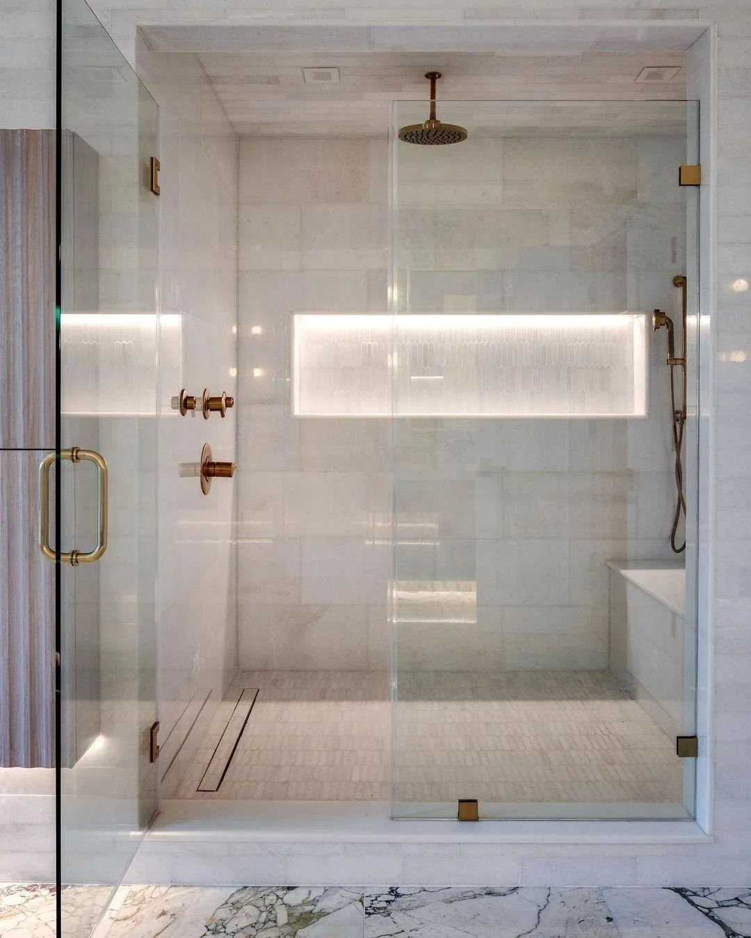 Glass walk-in shower with a rain showerhead, lit wall niche and brass fixtures
